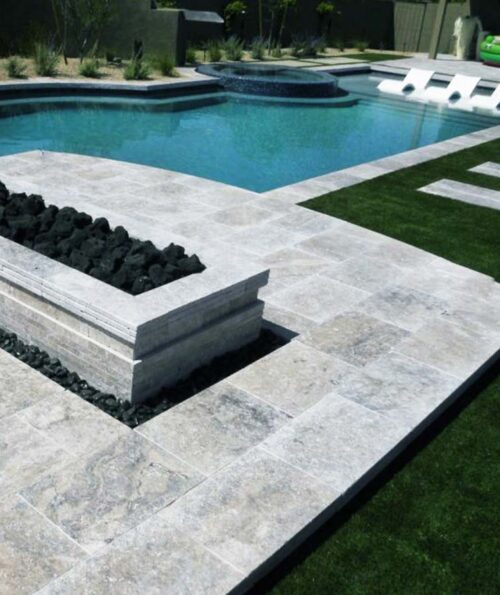Silver travertine tiles around a fire pit and pool area.